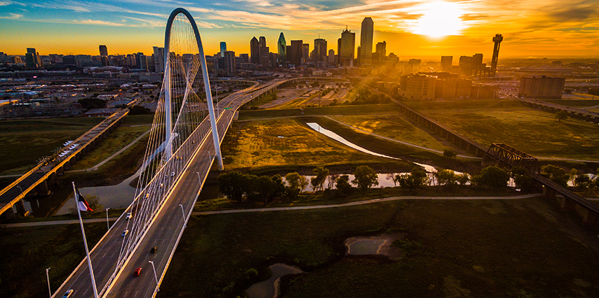 Aerial drone view high above Dallas , Texas landscape at perfect golden hour with sun rays across entire landscape - skyline cityscape in background with large suspension bridge - Margaret Hunt Hill Bridge
