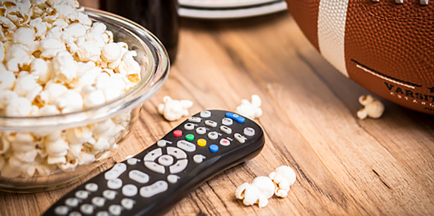 Football season is here.  Concept of sports fan watching the football game on TV at home, at tailgate party, or sports bar with snacks and drinks.  TV remote, popcorn, football and soda, beer bottles.  championship game party.